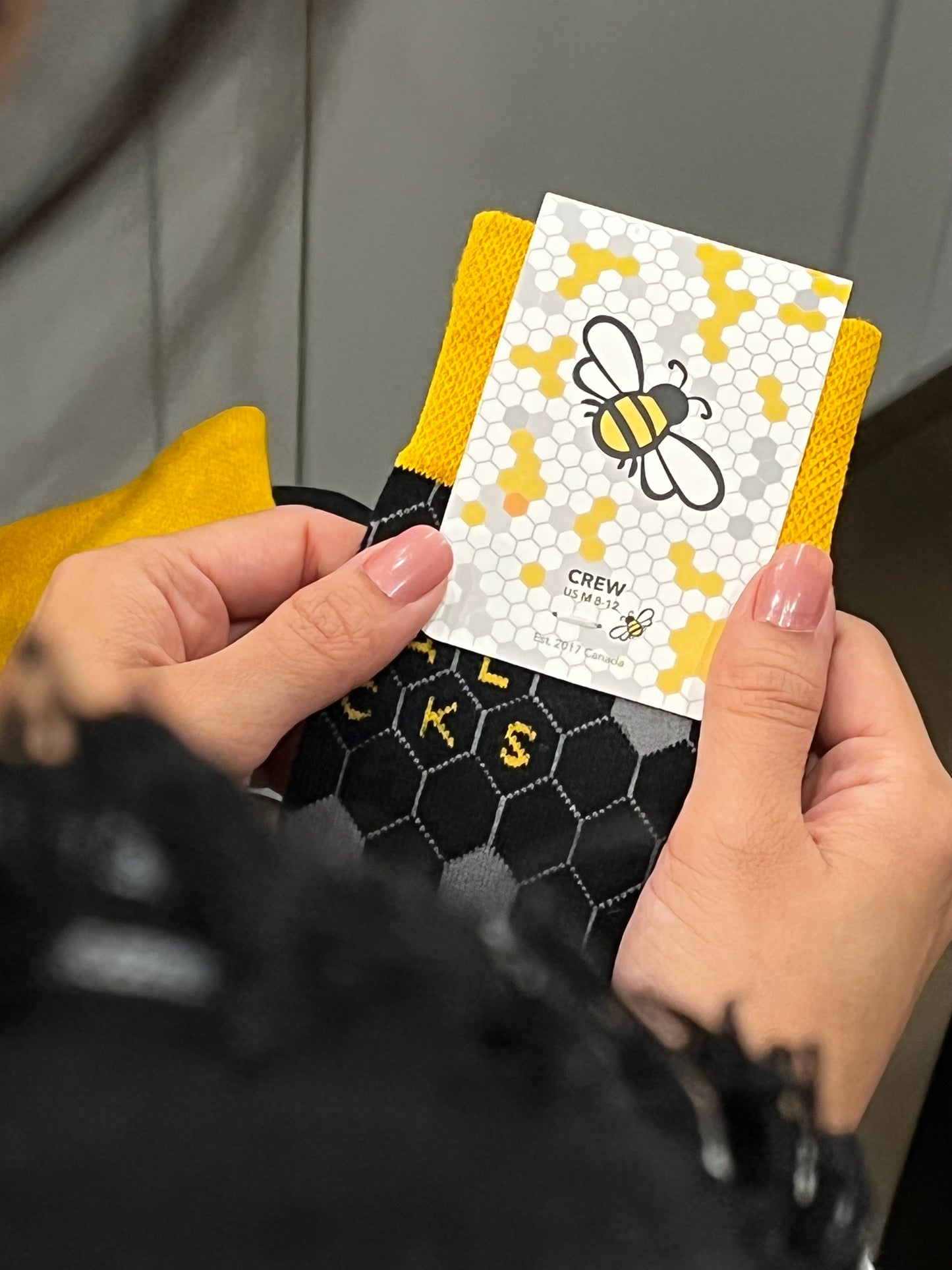 Person holding a small card with a bee design and yellow border. Halal Socks Honey Socks